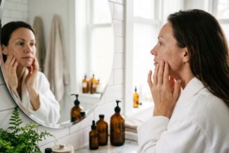 Femme aux traits fatigués examinant sa peau terne dans un miroir de salle de bain